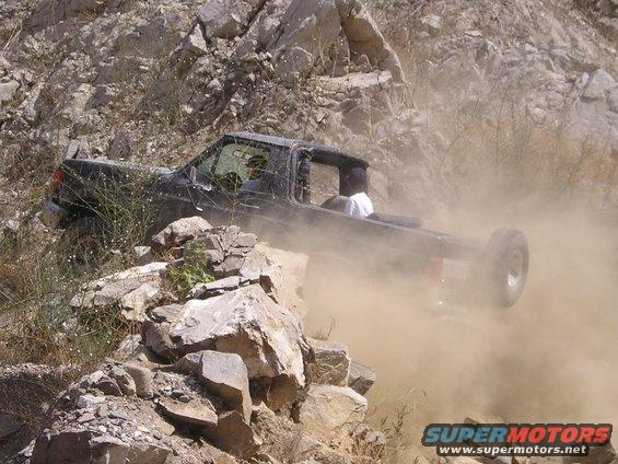 Black off-road vehicle kicking up dust on rocky terrain