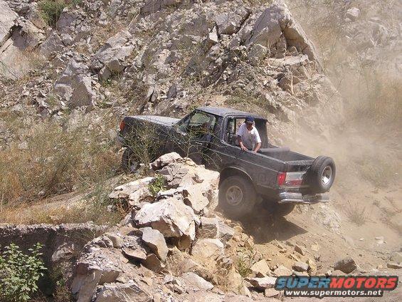 1989 Ford Bronco navigating a steep, rocky trail with a person in the driver's seat