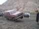 1989 Ford Bronco - A maroon Ford Bronco is stuck in the mud with its front wheel lifted, while another vehicle waits behind it.