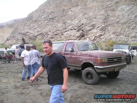 Maroon 1989 Ford Bronco parked in a dirt lot with people and other vehicles