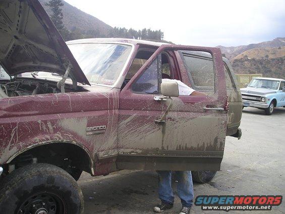 Muddy maroon SUV with door open, hood up. Another light blue truck is behind it