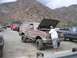 1989 Ford Bronco - A man inspects the engine of a dirty Ford Bronco parked outdoors with other vehicles and mountains in the background.