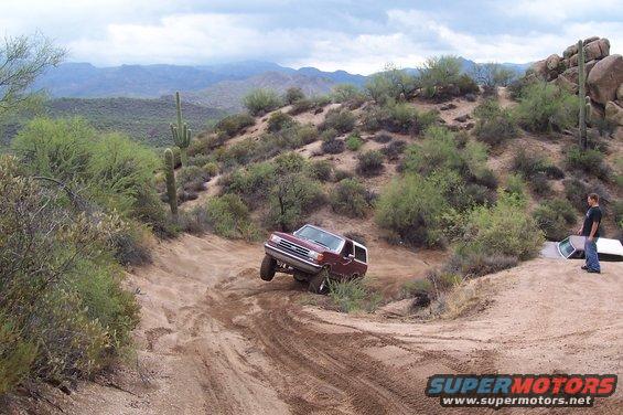 Maroon 1992 Ford Bronco driving off-road, with another vehicle partially visible on the right