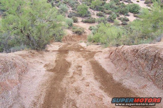 Dirt track going downhill through desert brush. Tire tracks visible