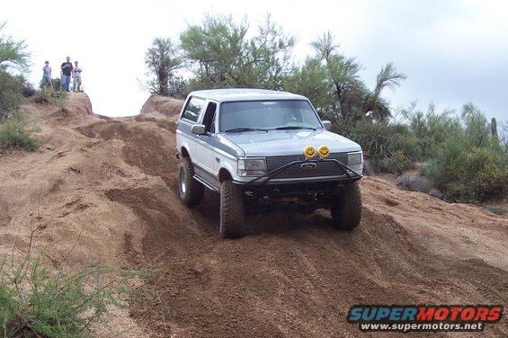 1992 Ford Bronco climbing a steep dirt hill with two people watching from the top