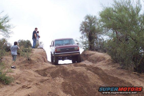 Maroon Ford Bronco climbing a dirt hill, front view. Off-road tires visible