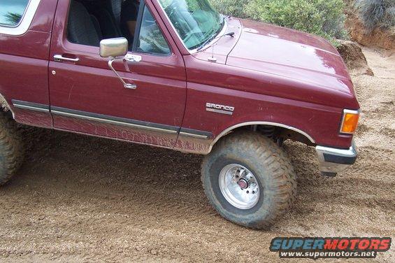 Maroon Ford Bronco on a dirt trail. Visible 'Bronco' badge on fender
