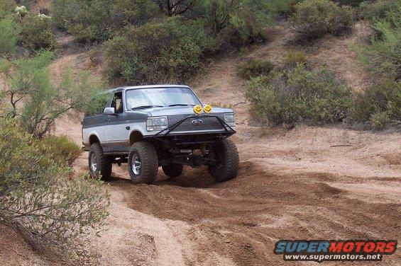 1992 Ford Bronco with lifted suspension and off-road tires driving on a dirt trail