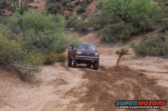 Maroon 1992 Ford Bronco driving on a dusty desert trail