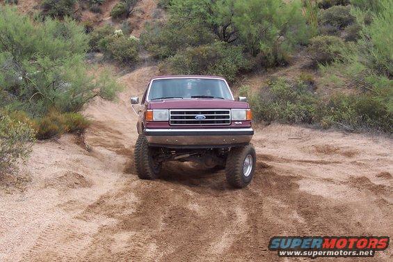 Maroon Ford F-Series truck with lifted suspension driving on a dirt trail