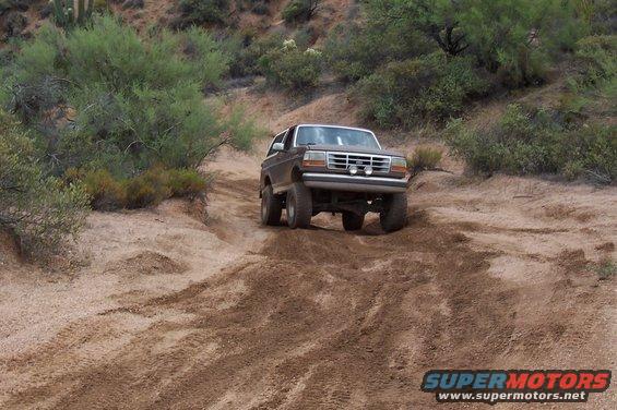 Brown 1992 Ford Bronco driving on a dirt hill with scrub brush and cacti