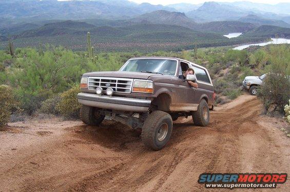 1992 Ford Bronco climbing a dirt hill with another SUV behind it in a desert landscape