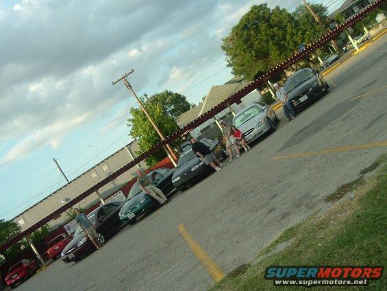Several cars parked in a lot with people standing around them