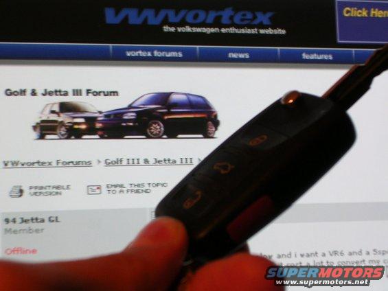 car key fob held over a computer screen showing a VWvortex forum page with images of a Golf and Jetta III