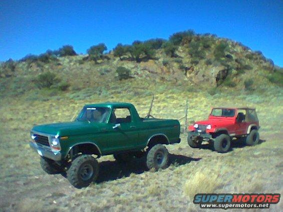Green 1978 Ford F-150 pickup truck with lifted suspension and off-road tires, parked next to a red Jeep