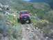 1979 Ford Bronco - Red Jeep Wrangler navigates a rough dirt path through a mountainous, brush-covered landscape.