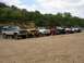 1967 Ford Bronco - A collection of SUVs are lined up on a gravel bar next to a river, with a dense tree line in the background.