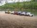 1967 Ford Bronco - Multiple Ford Broncos lined up on a gravel bar next to a river.
