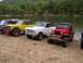 1967 Ford Bronco - A line of off-road vehicles are parked on a gravel bank next to a calm river with trees in the background.