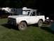 1967 Ford Bronco - A white 1967 Ford Bronco is parked on a grassy area with other vehicles and trailers in the background.