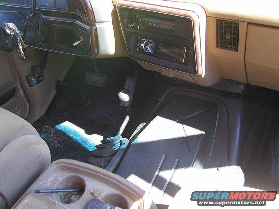 Car interior with tan dashboard, floor shifter, and center console. A radio is installed