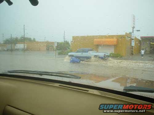 Light blue pickup truck driving through flooded street, water splashing