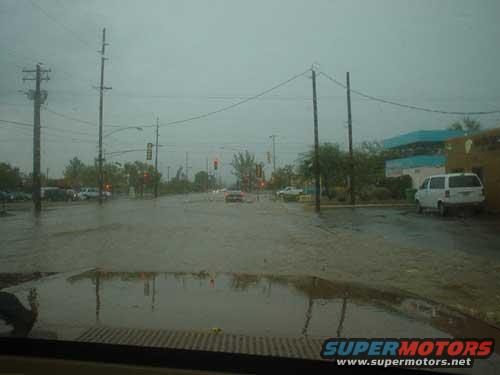 Flooded street with cars and a white van, viewed from inside a vehicle