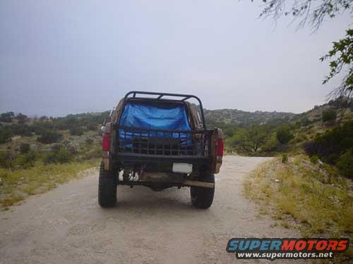 Rear view of a 1989 Ford Bronco on a dirt road with a blue tarp in the bed
