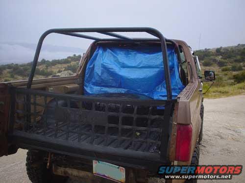 Brown Ford Bronco with a blue tarp covering the interior, seen from the rear