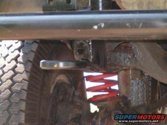 Undercarriage of a vehicle showing a red coil spring, tire tread, and metal frame