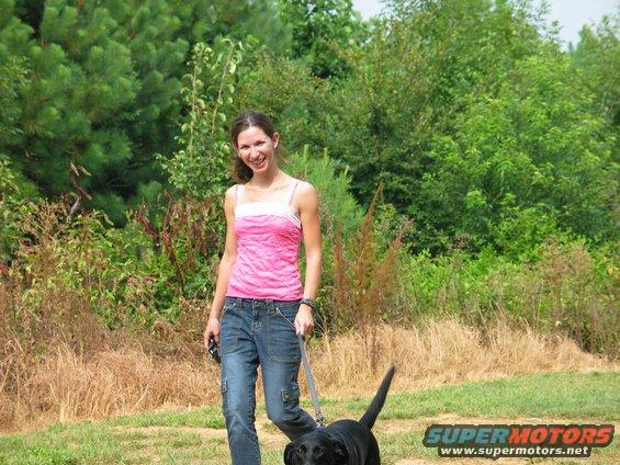 Woman walking black dog on leash outdoors with Supermotors logo