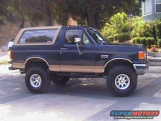 Side view of a dark blue and tan Ford Bronco with lifted suspension and chrome wheels