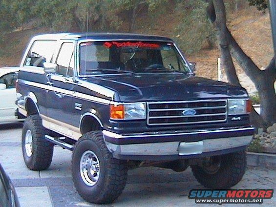 Lifted dark blue 1991 Ford Bronco with chrome wheels and a red Rockford Fosgate banner on the windshield