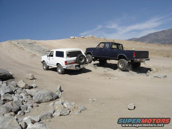 White 1988 Ford Bronco and blue Ford F-Series truck off-roading on a dirt trail