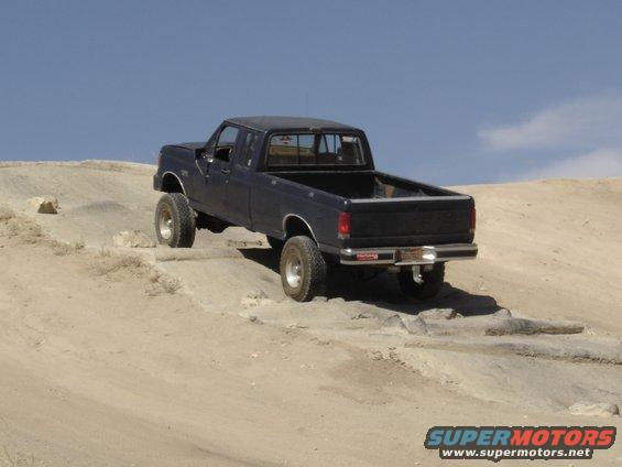 Dark blue pickup truck with lifted suspension driving on a dirt hill