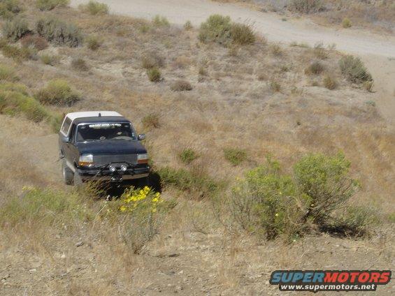 Dark blue 1992-1996 Ford Bronco with white camper shell driving on a dry, grassy hillside