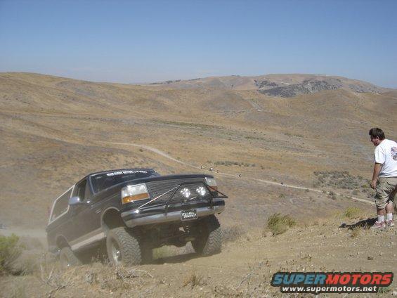 Black Ford Bronco with off-road tires and brush guard driving up a dusty hill, person watching