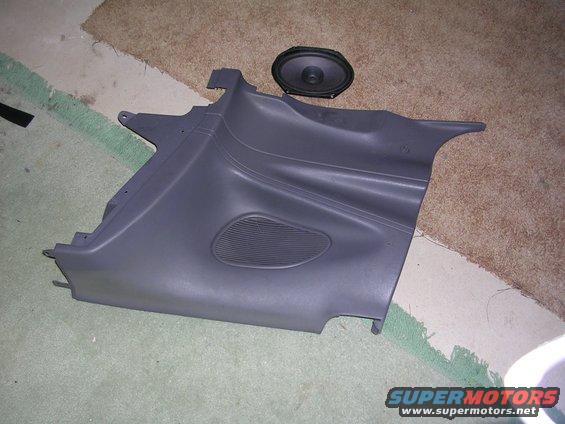 Gray plastic car door panel with speaker grille and separate oval speaker on carpet