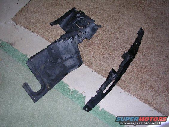 Two black plastic automotive underbody panels on a carpeted floor