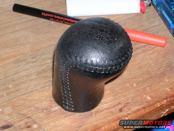 Leather-wrapped shift knob with visible stitching, lying on a wooden surface next to a pen and other objects