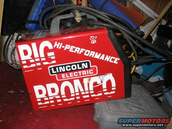 Red Lincoln Electric welding machine with 'BIG HI-PERFORMANCE BRONCO' text. It's sitting on a gray plastic case