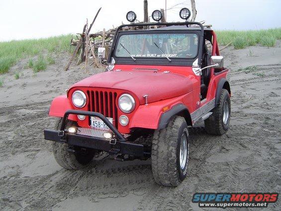 Red Jeep CJ-7 with aftermarket bumper and lights parked on sand dunes