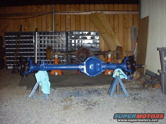 Blue painted vehicle axle on stands, with another rusty axle behind it
