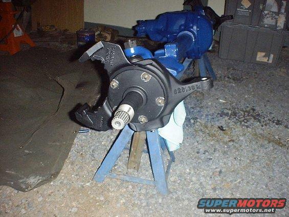 Black painted vehicle spindle assembly on blue jack stands. Some blue painted differential housing is visible behind it