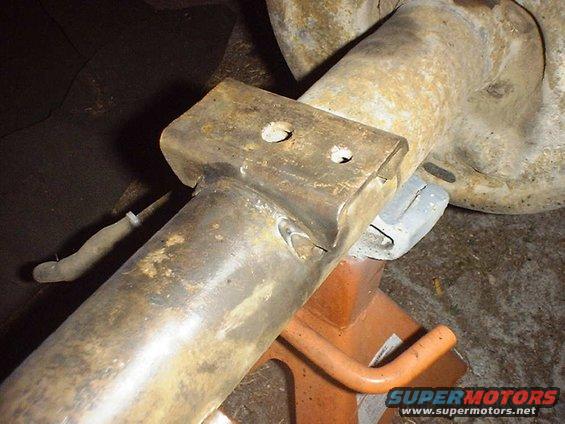 Rusty rear axle assembly on an orange jack stand, showing a metal bracket with two holes