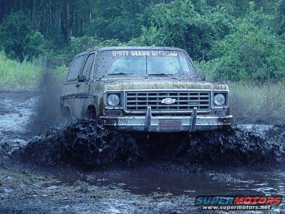 Brown Chevrolet K5 Blazer driving through mud, "DIRTY DEEDS OFFROAD" on windshield