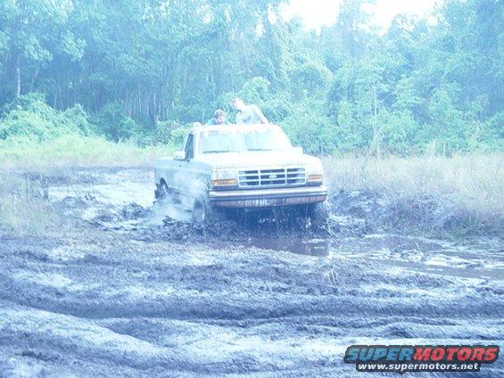 Ford pickup truck driving through mud, two people in the cab