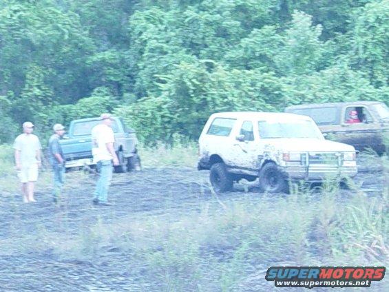 Mud-splattered white Ford Bronco parked off-road with a brush guard