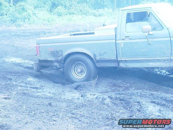 Ford F-Series truck with rear wheel stuck in mud, driving through a muddy field