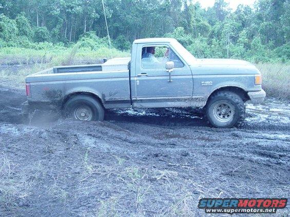 Gray Ford F-150 pickup truck stuck in mud, side view. The truck has a toolbox in the bed and off-road tires